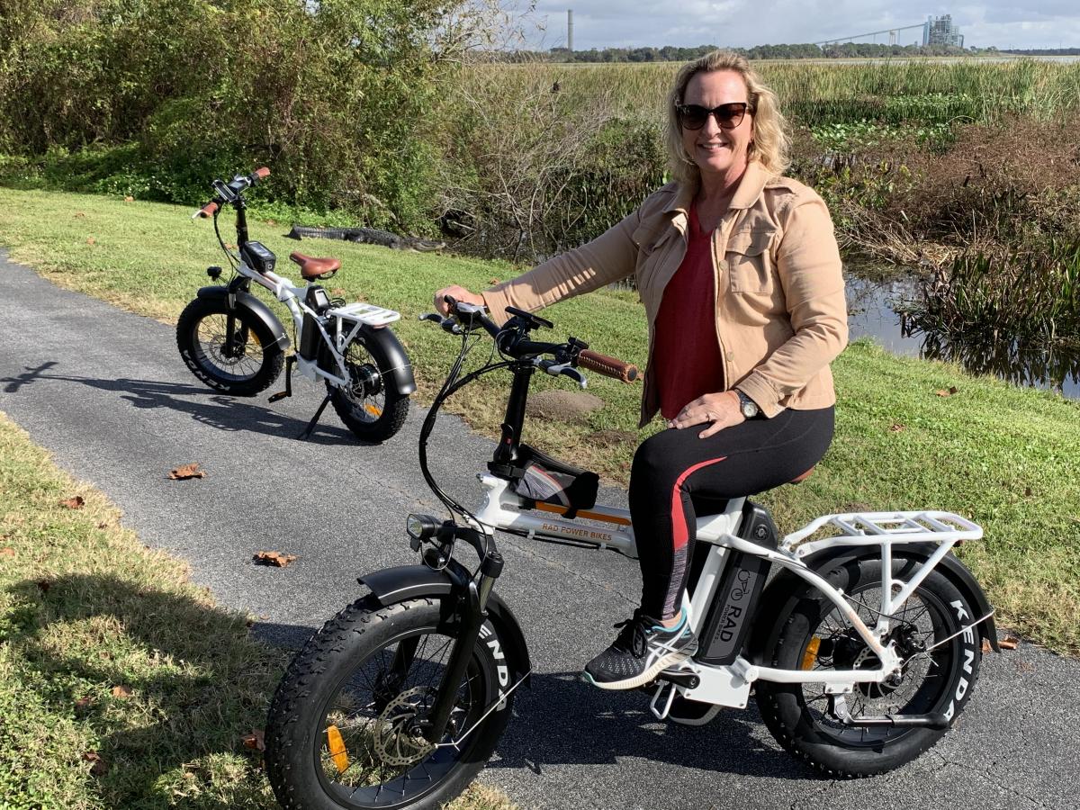 Wife and I on electric bikes with gator in the background